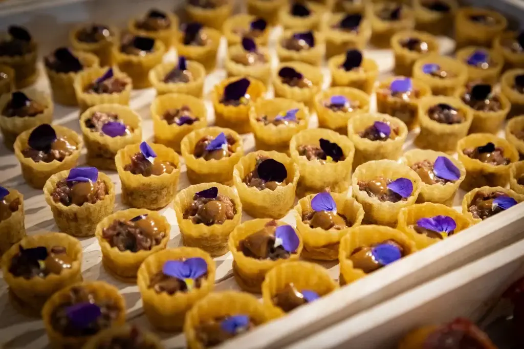 A tray of tartlet canapés topped with edible flowers and colourful garnishes.