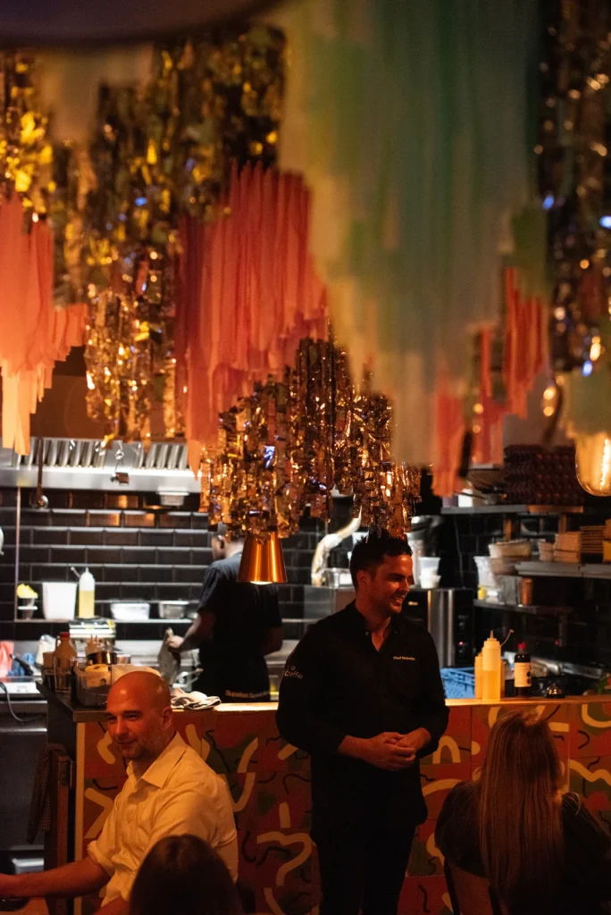 Nick Rapson speaking with guests in a warmly lit dining room.